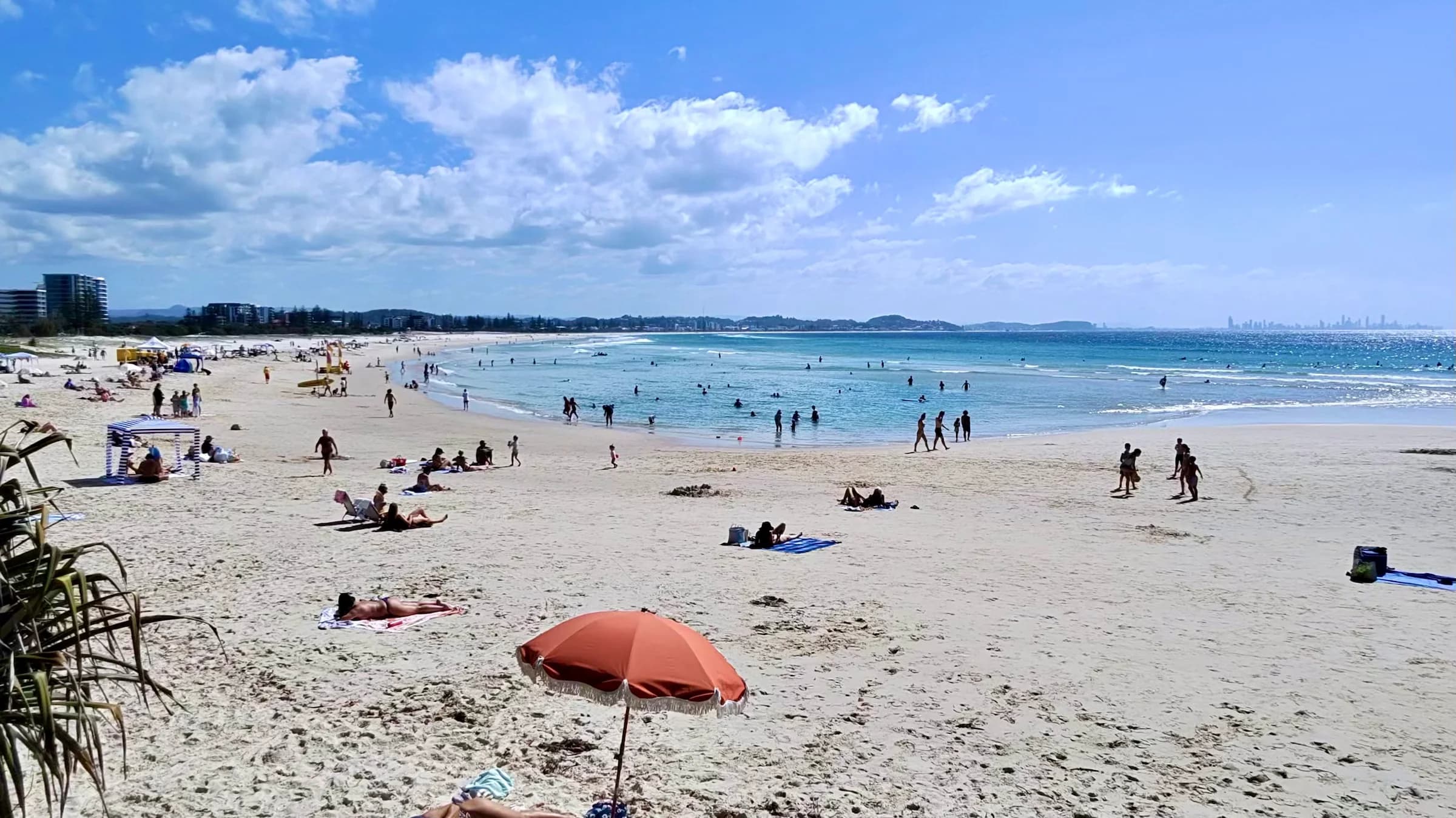 Busy Australian beach with swimmers between distant red and yellow surf flags marking the safe-swimming zone