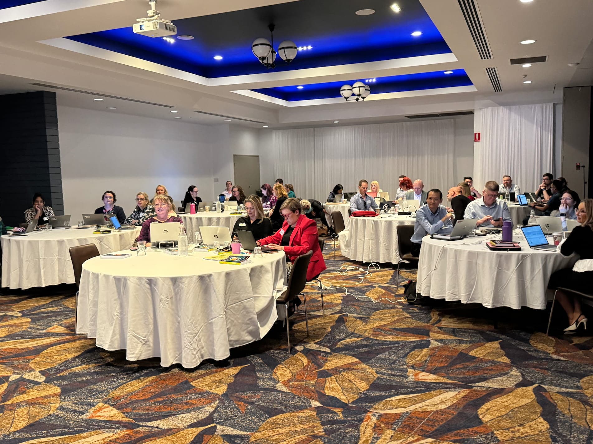 Wide view of the Practical AI workshop room at Springlake Hotel, members at round tables with laptops open