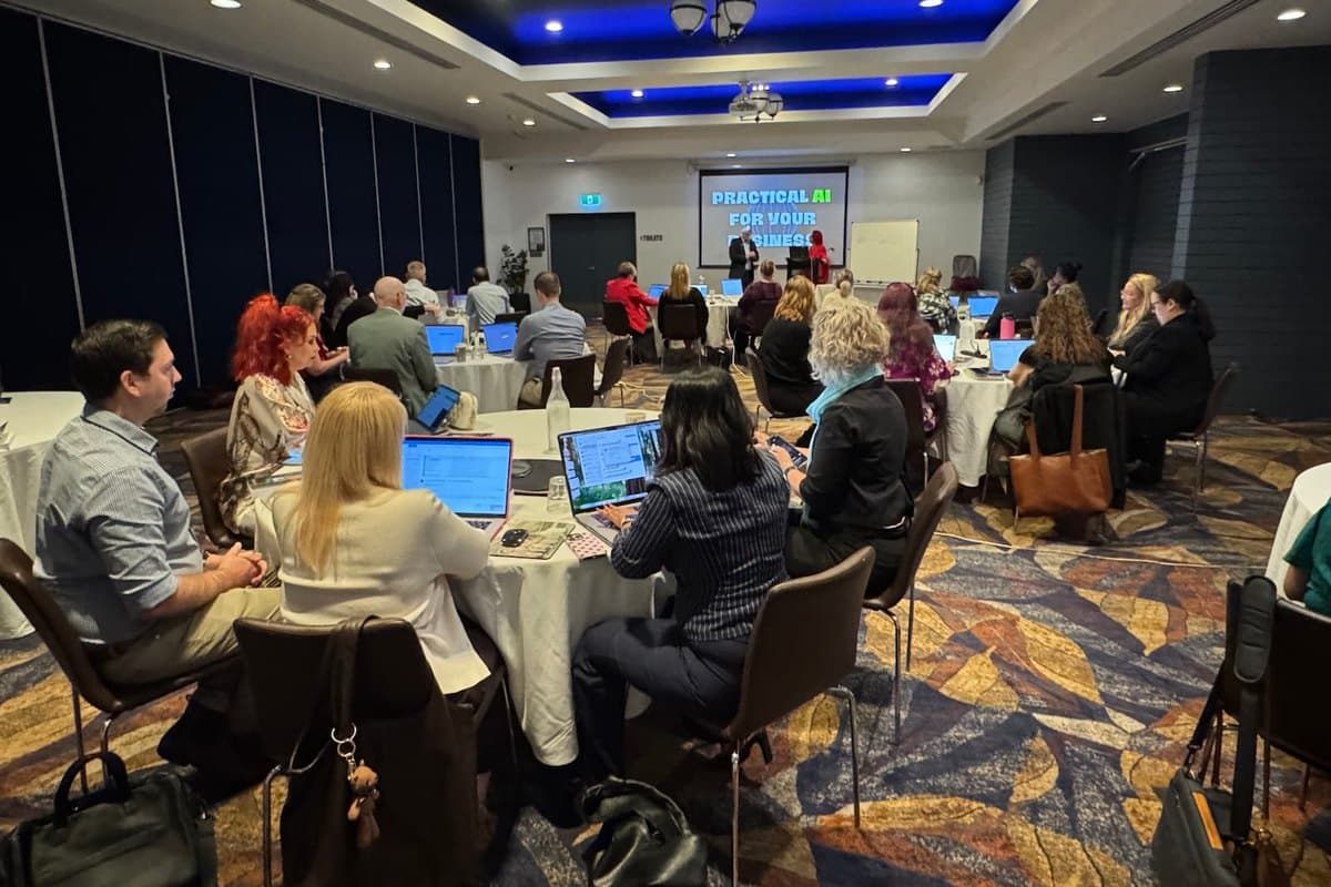 Participants at round tables with laptops open during one of Tracy Sheen's practical AI sessions.