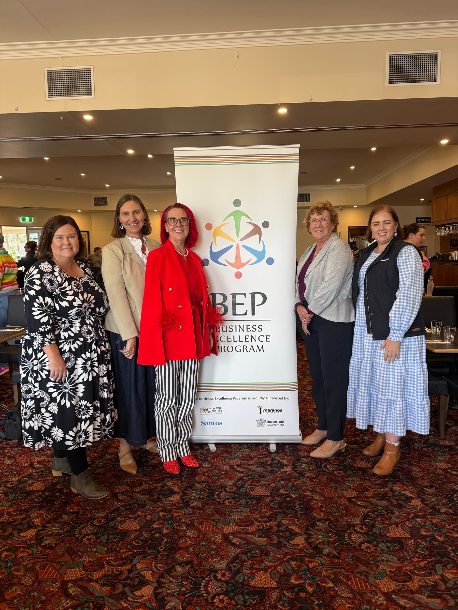 Tracy Sheen with the Business Excellence Program team in front of the BEP banner at the Roma Explorers Inn